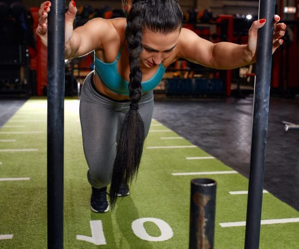 Beautiful young woman with barbell weight plate working out in sports club.