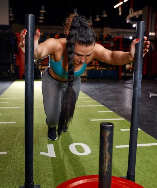 Beautiful young woman with barbell weight plate working out in sports club.